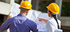 Two people in hard hats looking over a blueprint